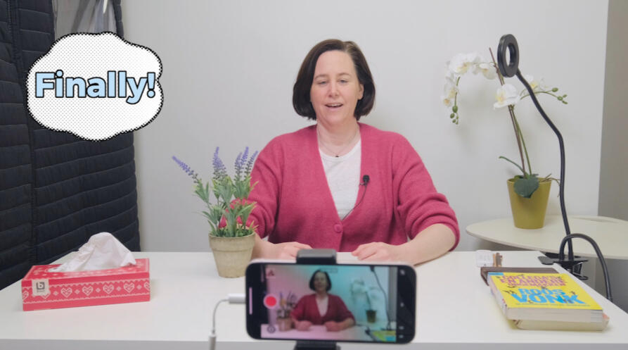 Sarah Martens sitting behind a smartphone camera looking relieved and saying "finally!"